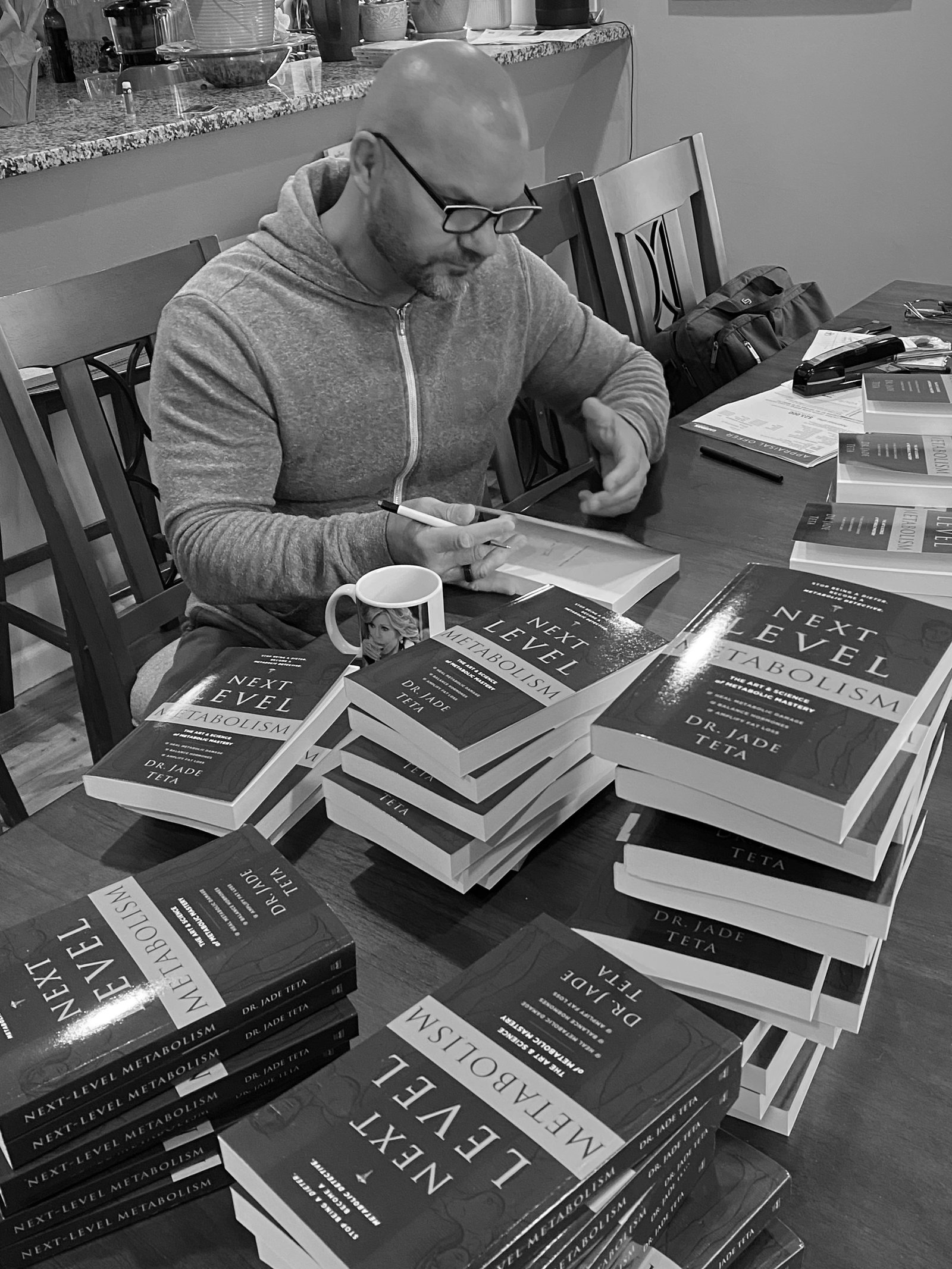 Signing a stack of Next Level Metabolism at the kitchen table.